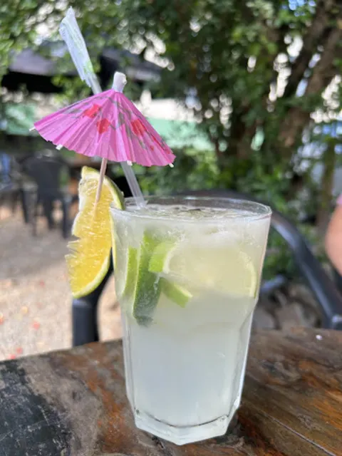 Copo de caipirinha de limão com gelo e sombrinha de papel, na mesa do quintal