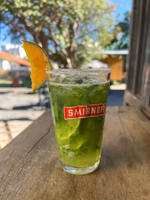 Copo de caipirinha verde de rúcula com limão, borda de sal e fatia de laranja