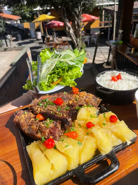 Costela assada na chapa com mandioca, arroz e salada, na mesa do quintal