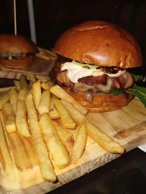 Hambúrguer de pão brioche com bacon e molho branco, na tábua com batata frita