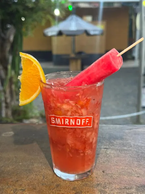 Copo de caipiroska vermelha com morango macerado, rodela de laranja e um picolé rosa espetado