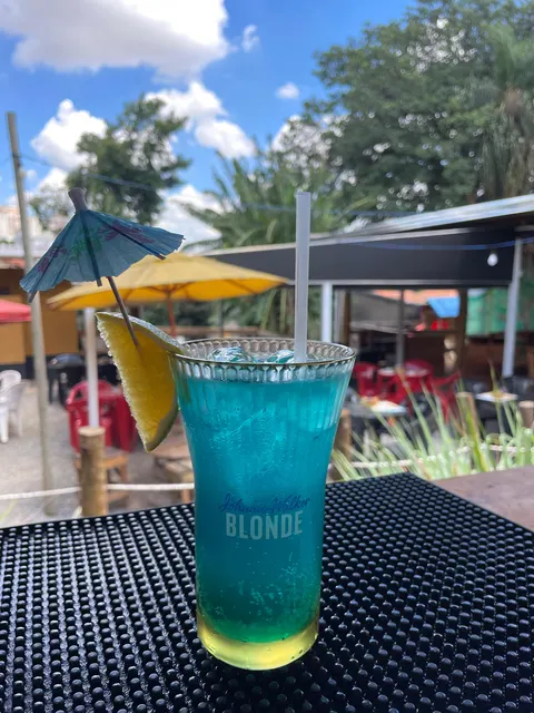 Copo de drink azul-turquesa com fatia de laranja, nas mesas ao ar livre