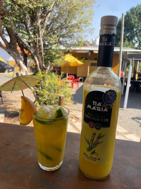 Copo de caipiroska de milho verde ao lado da garrafa, na mesa do quintal