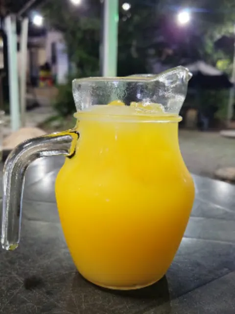 Jarra de vidro cheia de suco de laranja, com canudo, na mesa do quintal